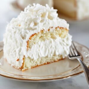 Coconut Cloud Cake on a stand with slice removed showing creamy layers